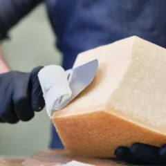 Mână cu mănușă neagră tăind o brânză mare cu un cuțit