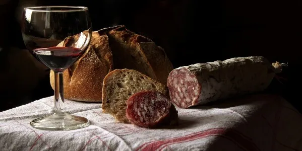 Salam uscat, pâine și un pahar de vin roșu pe o față de masă